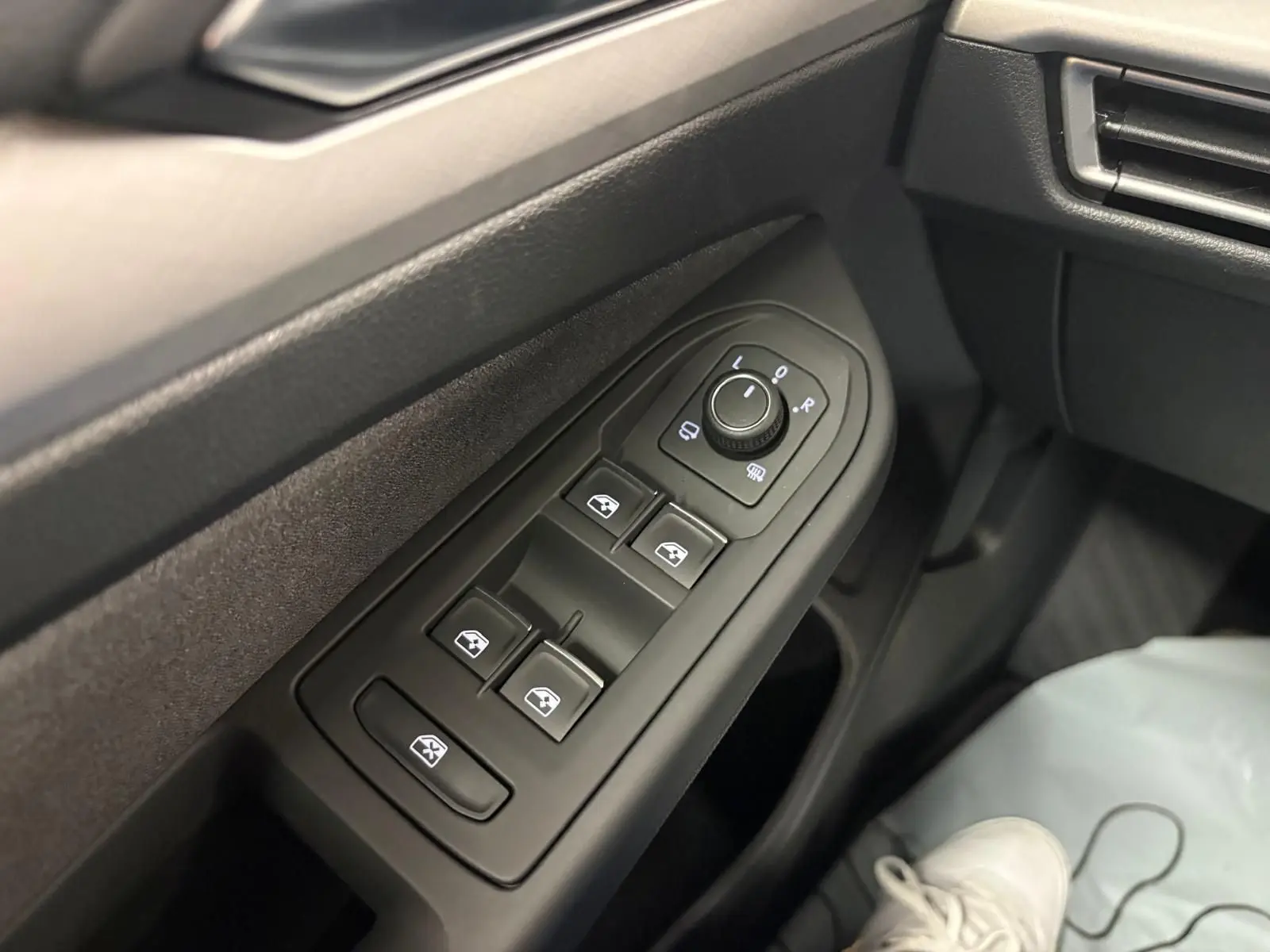 Gros plan sur les commandes des vitres électriques et des rétroviseurs côté conducteur dans l’habitacle noir d’une Volkswagen Golf 2025.