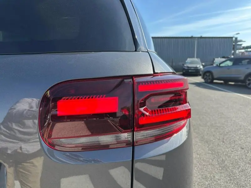 Gros plan sur le feu arrière droit rouge du Citroën C5 Aircross 2025 gris Platinium, avec reflet de l'environnement urbain.
