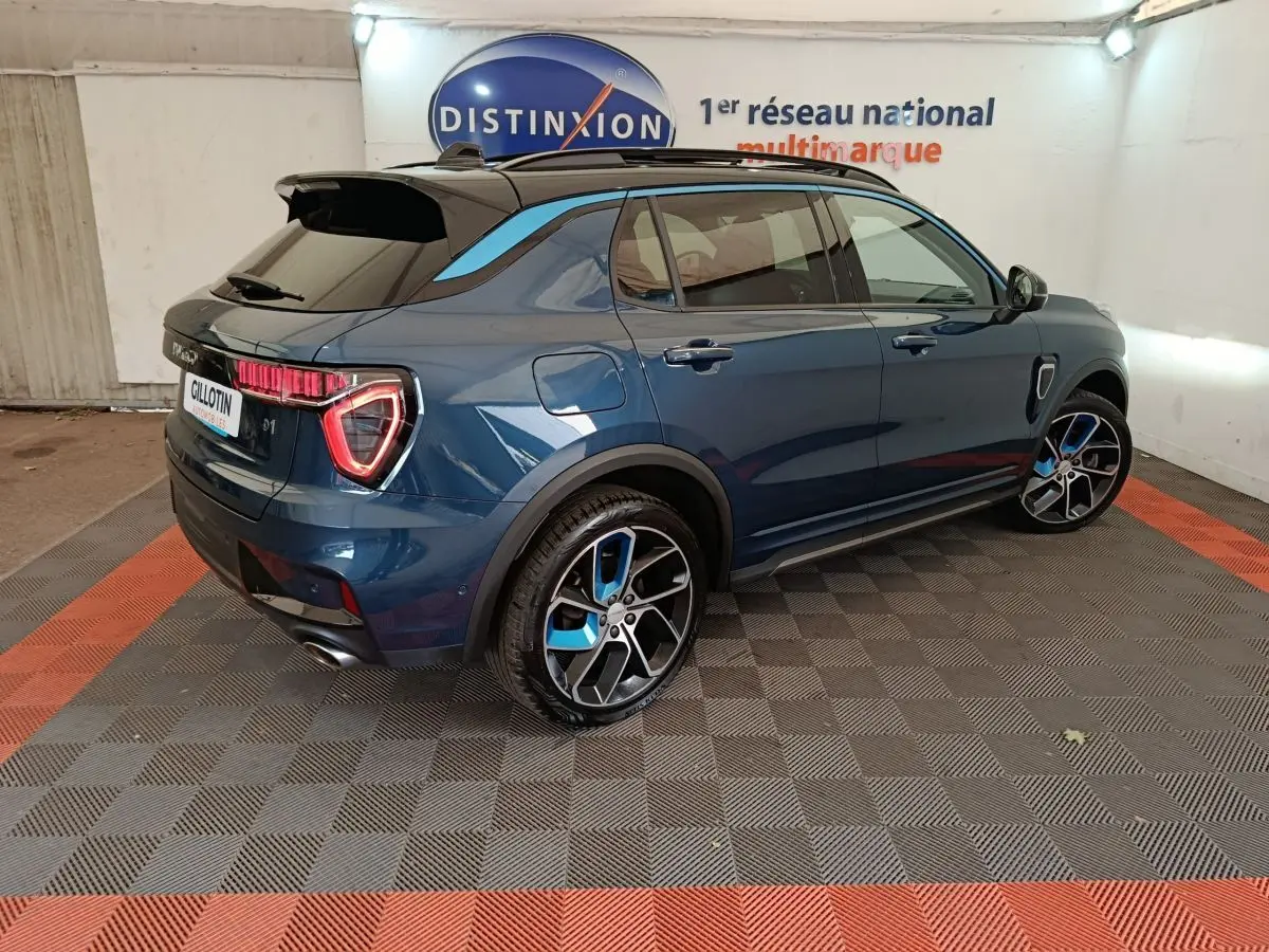 Vue 3/4 arrière droite d'un SUV Link & Co 01 bleu avec jantes bicolores et toit noir dans un garage.