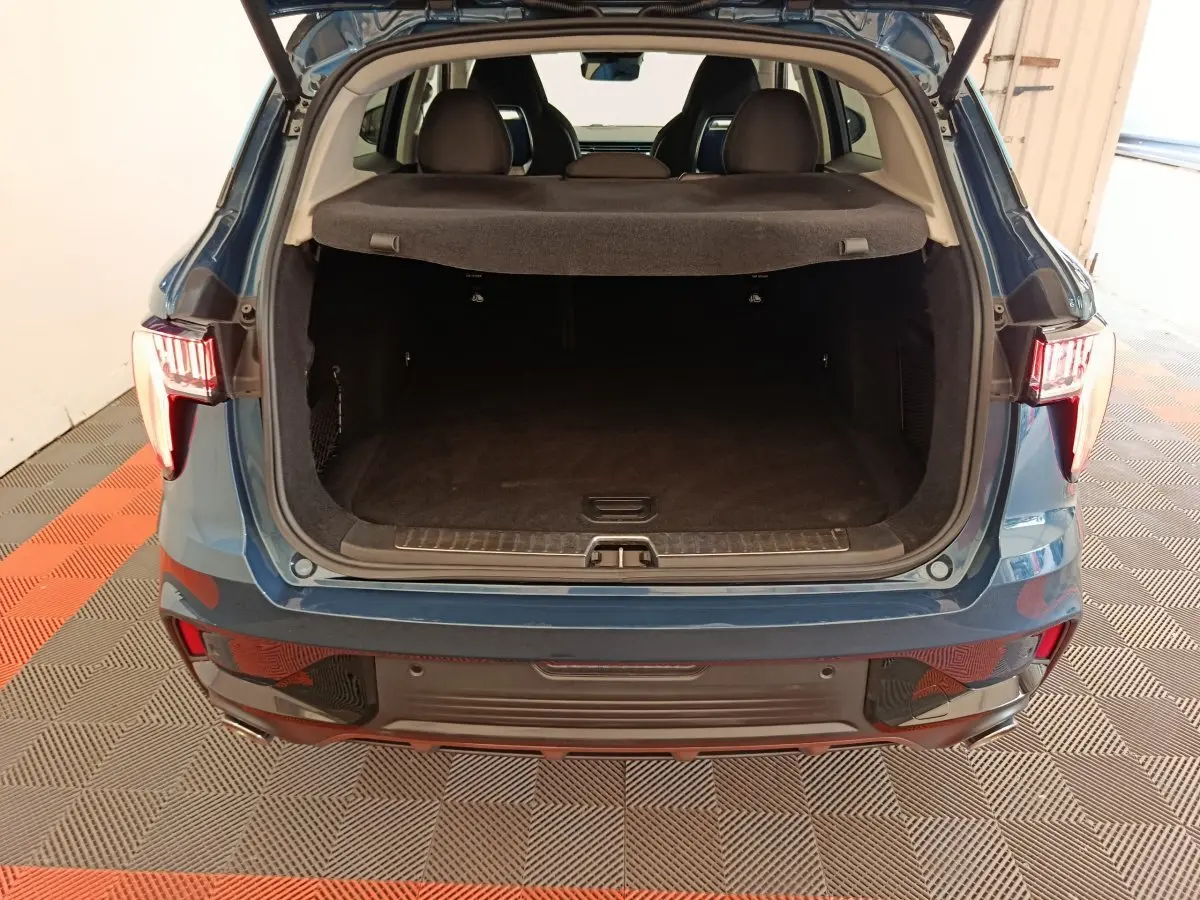 Vue arrière du coffre ouvert du SUV bleu LINK & CO 01 hybride rechargeable, intérieur spacieux et tapis noir visible.