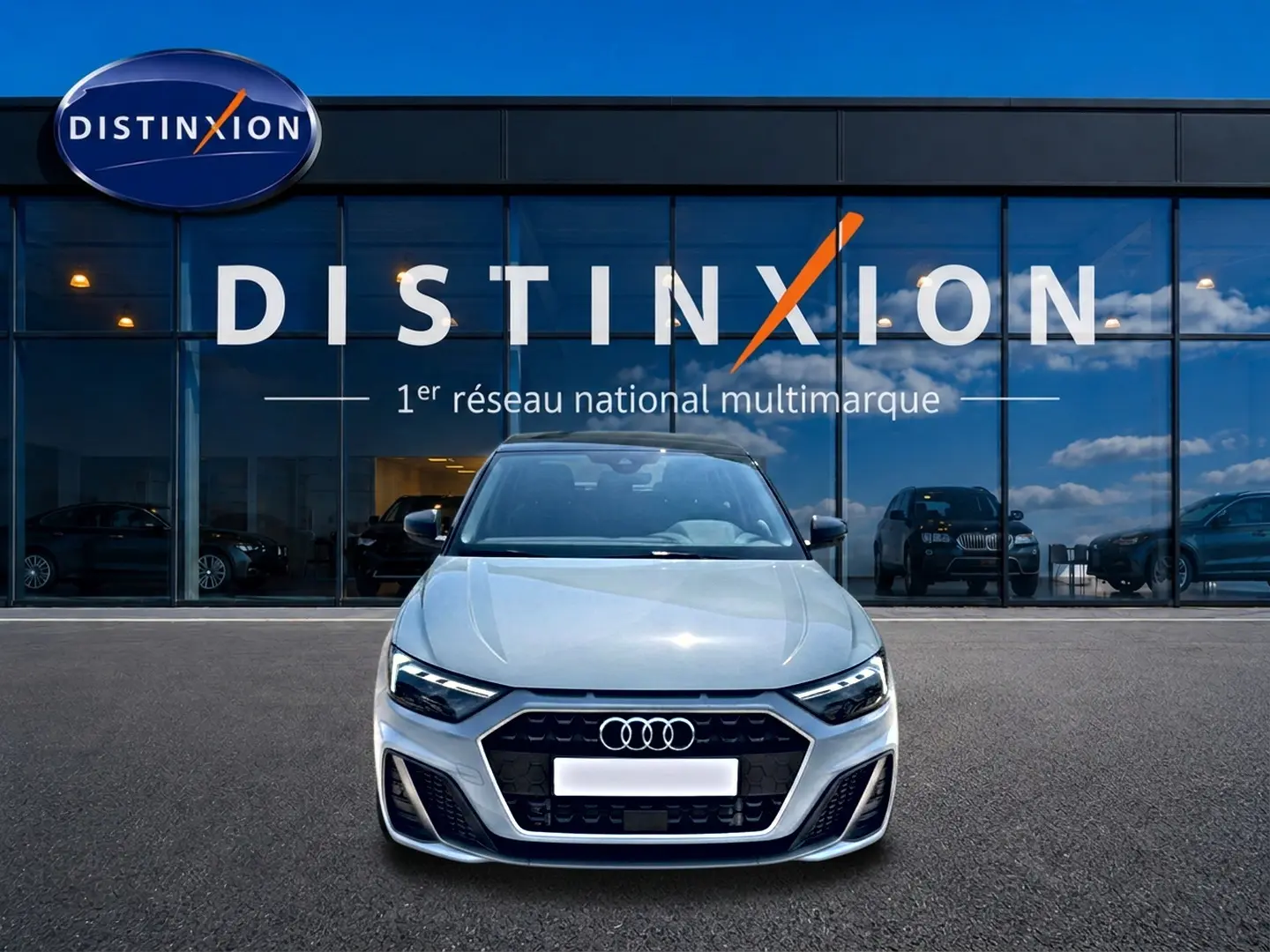Vue avant d'une Audi A1 Sportback 30 TFSI 116 S line gris arrow avec calandre noire et phares LED devant un showroom Distinxion.