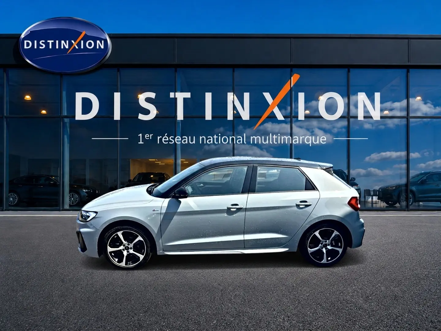 Profil droit d'une Audi A1 Sportback gris arrow avec toit noir, jantes alu et détails S line devant une vitrine Distinxion.