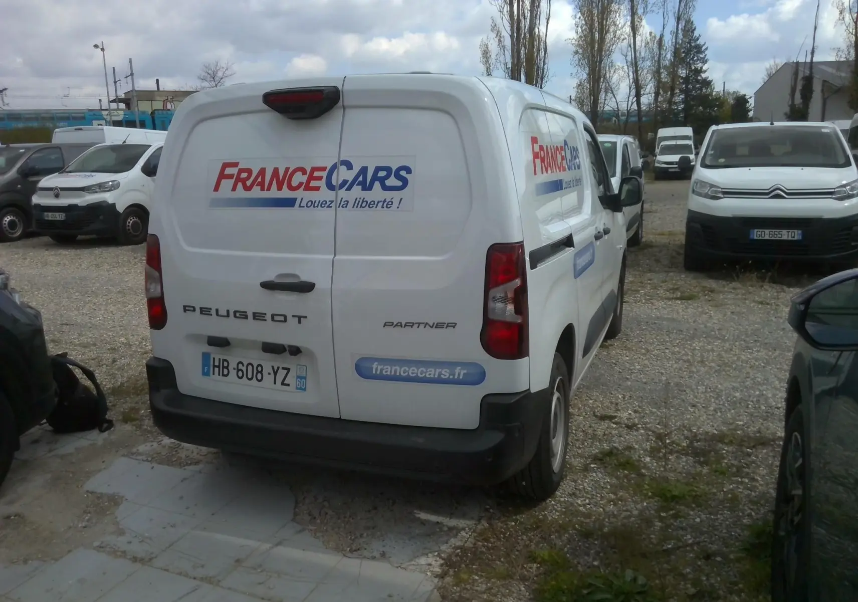 Vue 3/4 arrière droite d'un Peugeot Partner blanc avec logo France Cars et slogan "Louez la liberté" sur les portes arrière.
