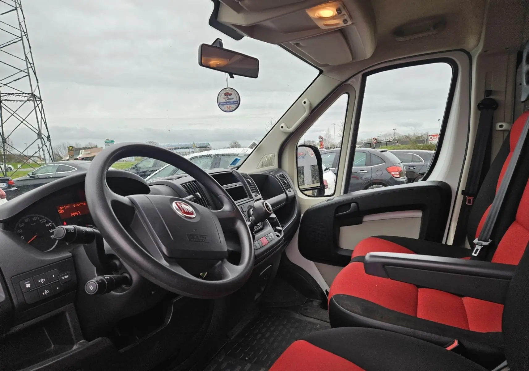 Vue intérieure côté conducteur du Fiat Ducato Combi 2014 avec sièges rouge et noir et tableau de bord noir.