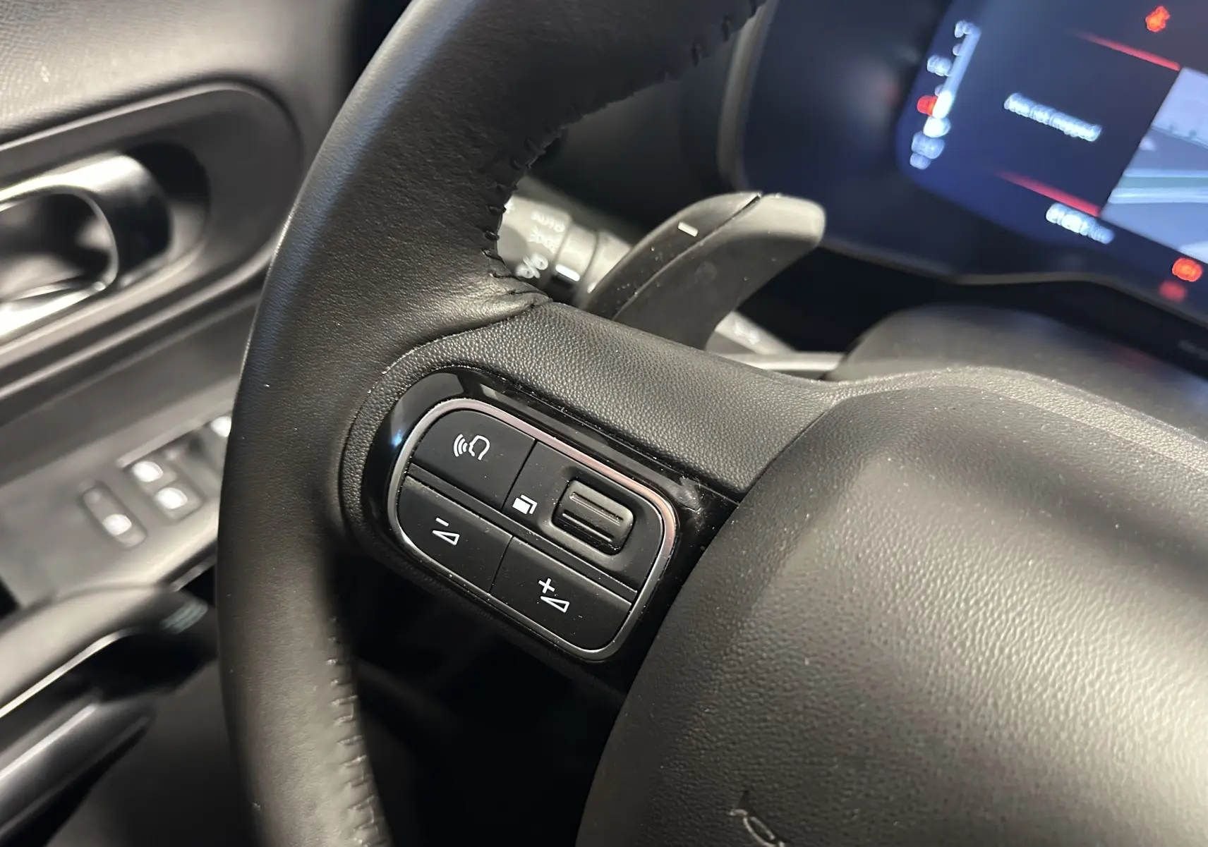 Gros plan sur le volant en cuir noir du Citroën C5 Aircross hybride 2025, avec commandes intégrées et tableau de bord numérique en arrière-plan.