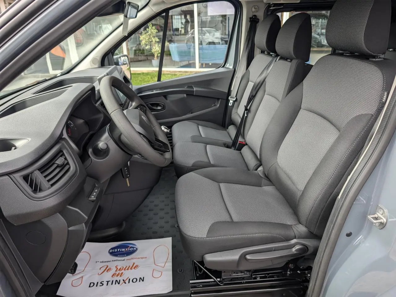Vue intérieure côté conducteur du Renault Trafic Fourgon gris, montrant les sièges tissu gris et le tableau de bord.