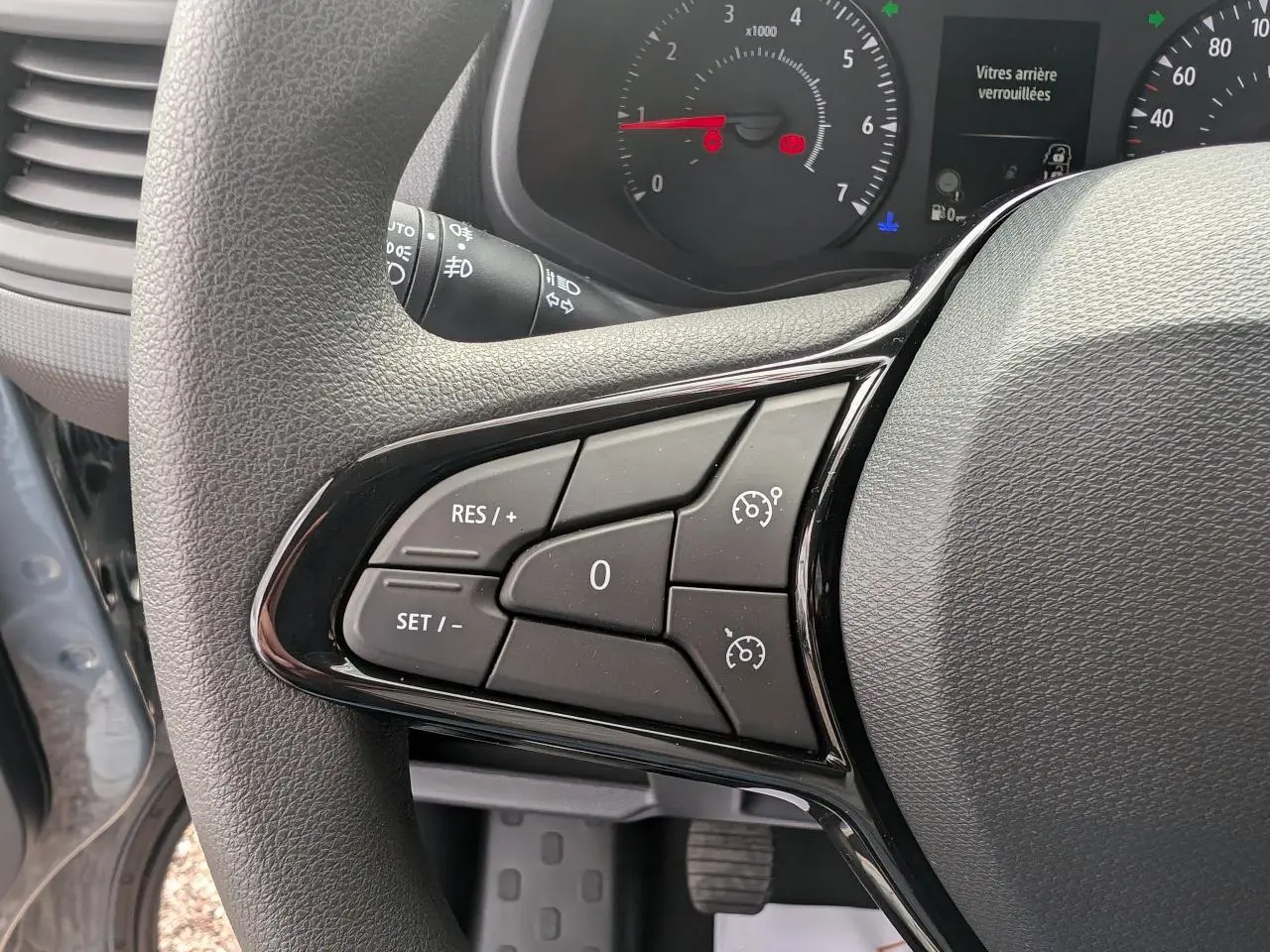 Gros plan sur les commandes de régulateur de vitesse au volant du Renault Trafic Fourgon gris, tableau de bord en arrière-plan.