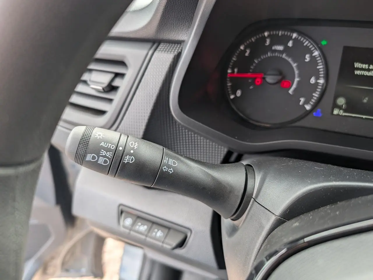 Gros plan sur la commande des feux et clignotants à gauche du volant du Renault Trafic Fourgon gris, tableau de bord visible.