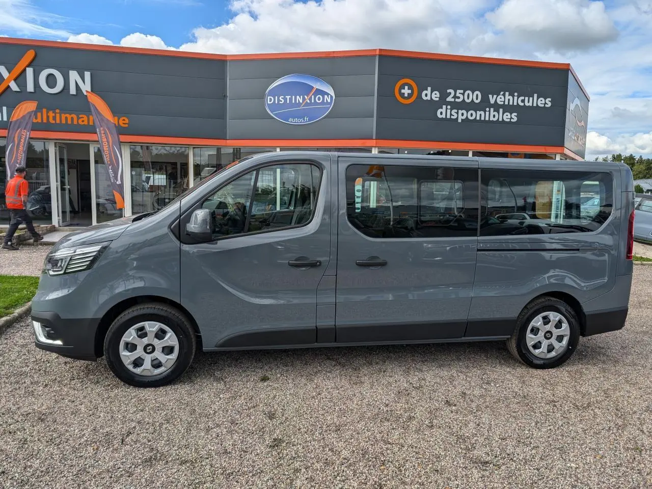 Profil droit du Renault Trafic Fourgon gris, version L2, avec grandes fenêtres latérales et jantes argentées.