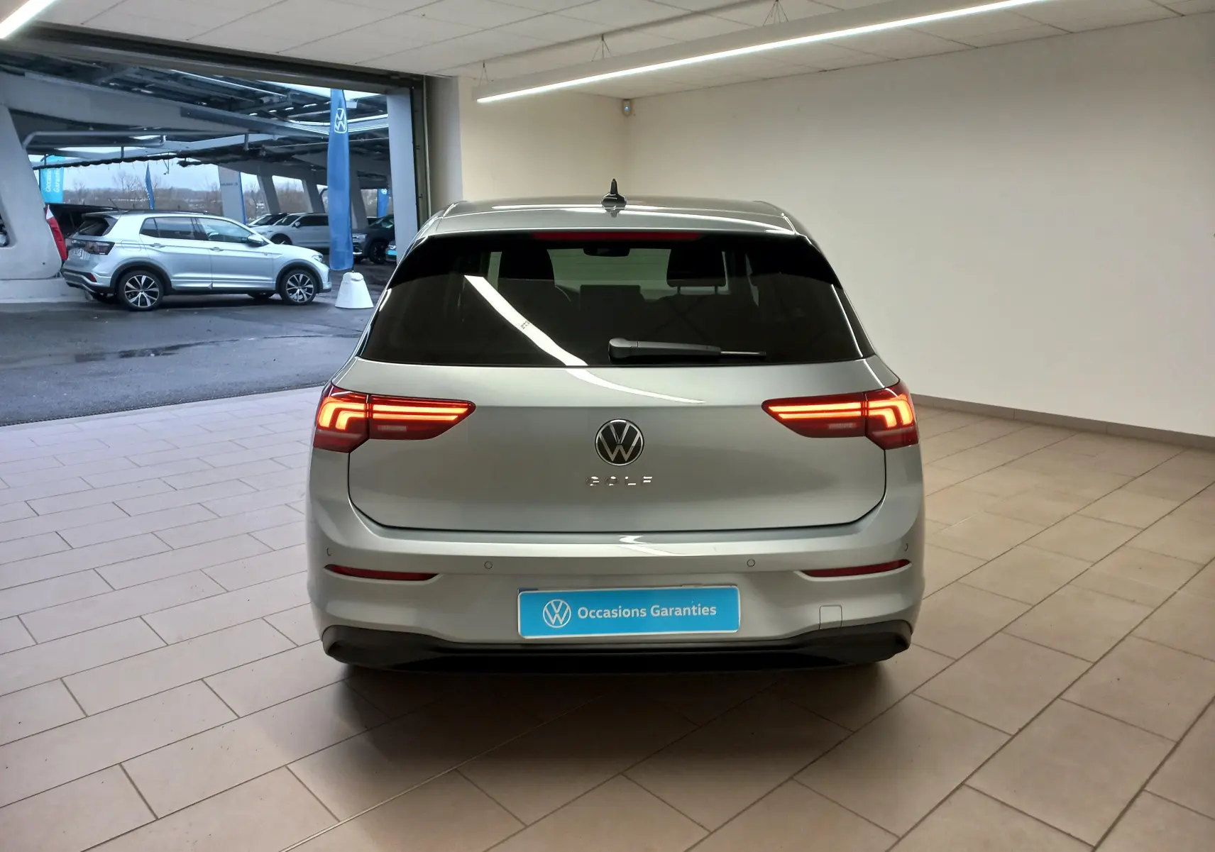 Vue arrière d'une Volkswagen Golf 2025 argent Dolomite avec feux LED allumés dans un showroom.