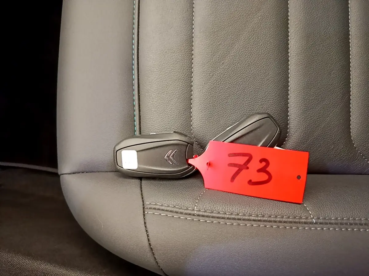 Gros plan sur la clé noire Citroën avec étiquette rouge posée sur un siège en cuir gris foncé.