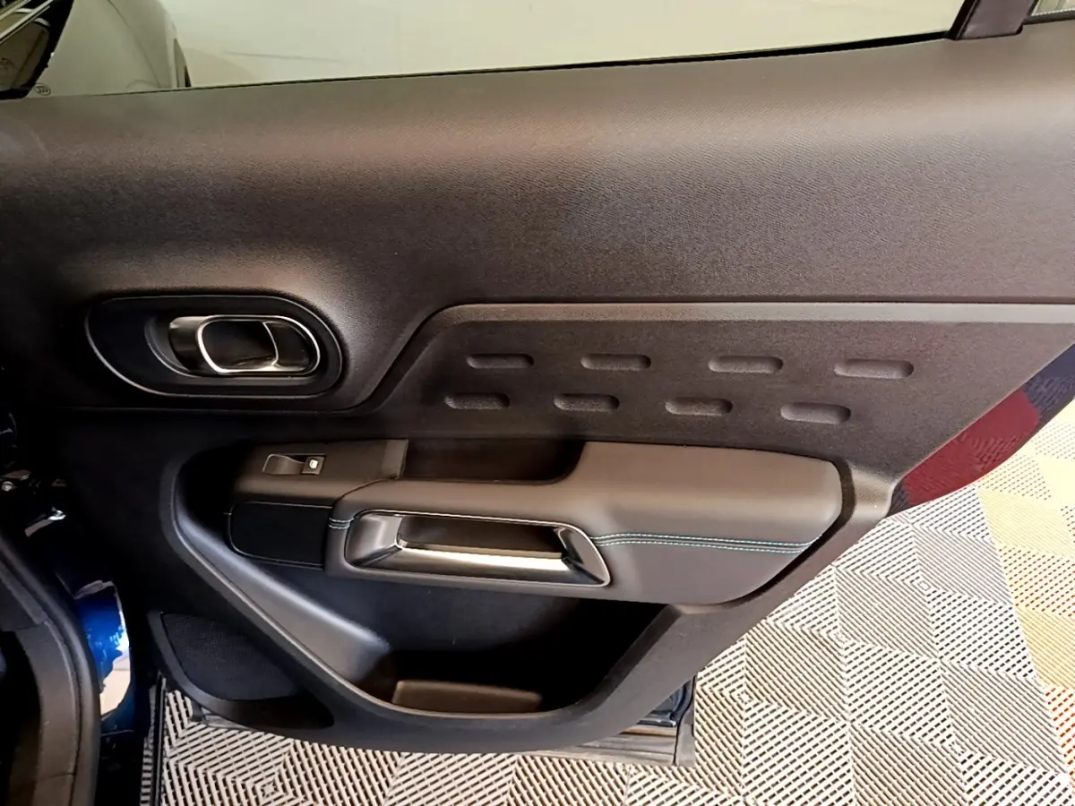 Gros plan sur la porte intérieure côté gauche du Citroën C5 Aircross 2023, finition noire avec surpiqûres bleues.