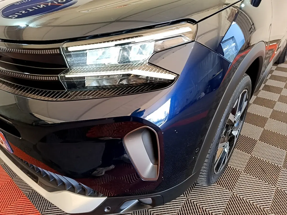 Gros plan sur l'avant droit bleu foncé du Citroën C5 Aircross 2023, mettant en valeur le phare LED et la prise d'air.