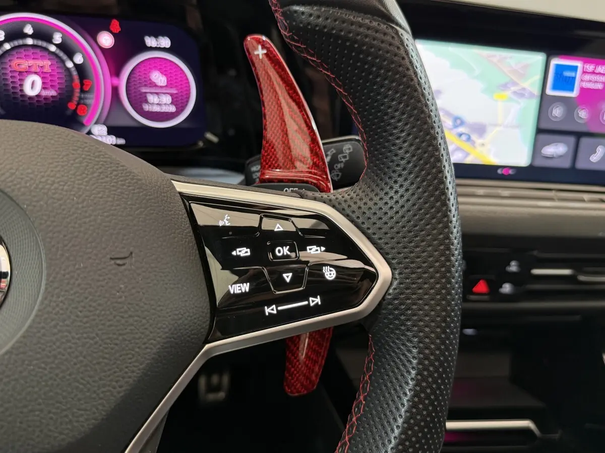 Gros plan sur le volant cuir perforé avec palettes rouges et affichage numérique violet de la Volkswagen Golf GTI Clubsport 2022.