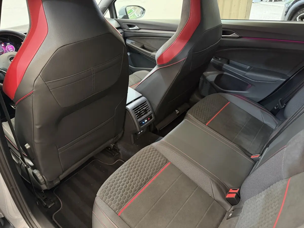 Vue arrière intérieure de la Volkswagen Golf GTI Clubsport 2022, sièges noirs avec surpiqûres rouges et ambiance lumineuse violette.