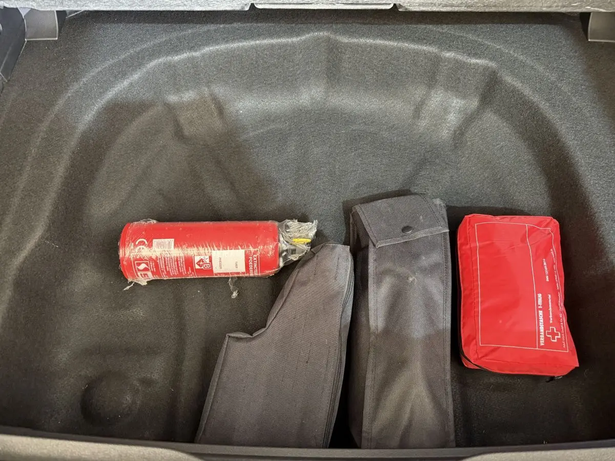 Coffre ouvert d’une Volkswagen Golf gris foncé, vue plongeante sur extincteur, trousse de secours et housses noires.