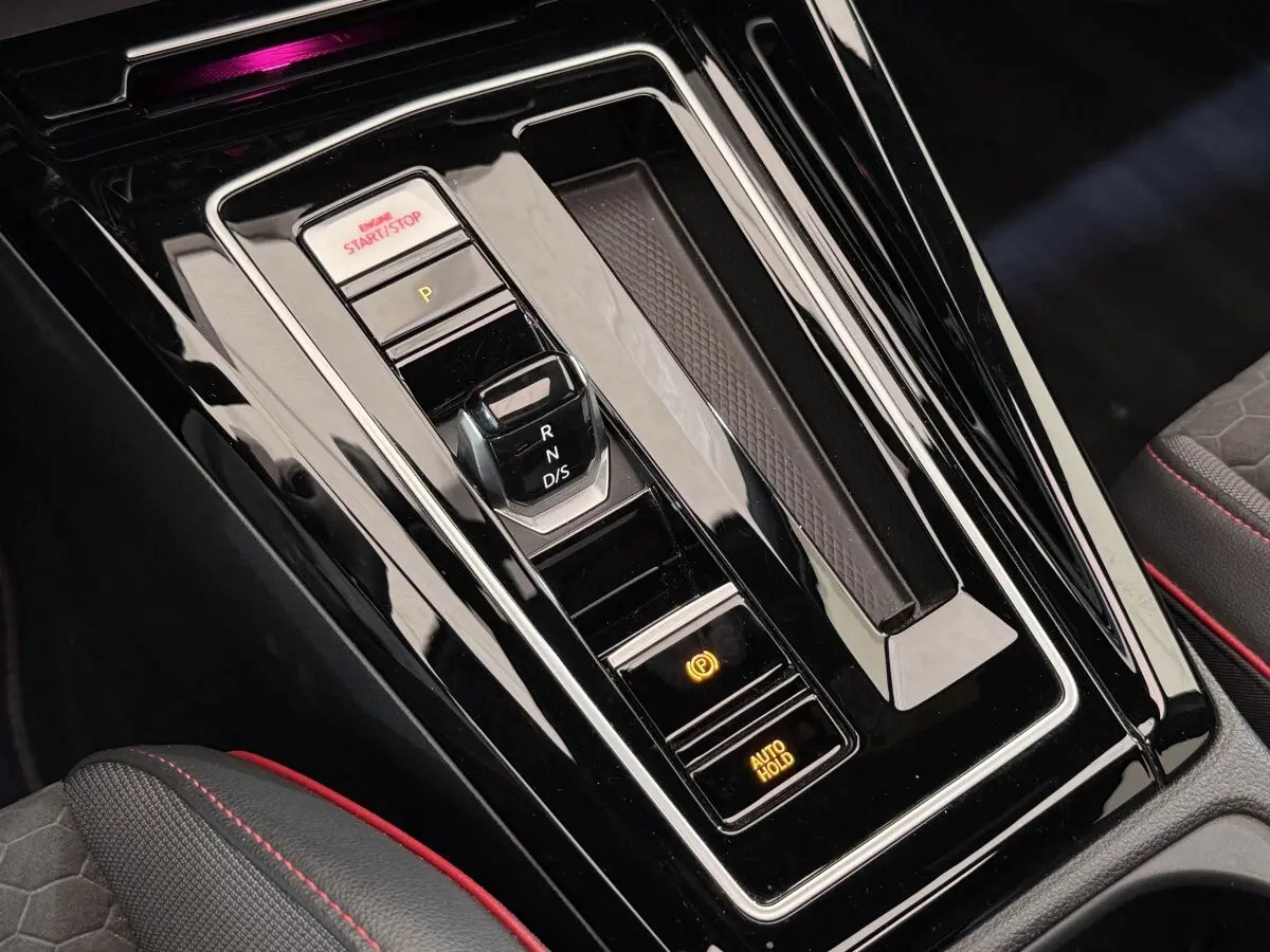 Gros plan sur la console centrale noire brillante avec levier de vitesses et boutons start/stop d’une Volkswagen Golf gris foncé.