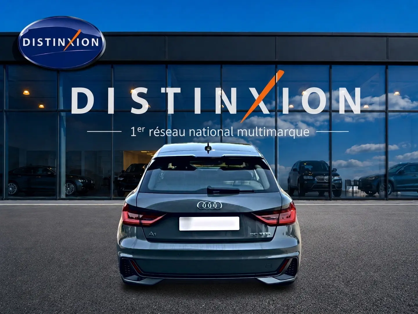 Vue arrière d'une Audi A1 Sportback gris chronos avec feux LED et diffuseur noir, stationnée devant une vitrine Distinxion.