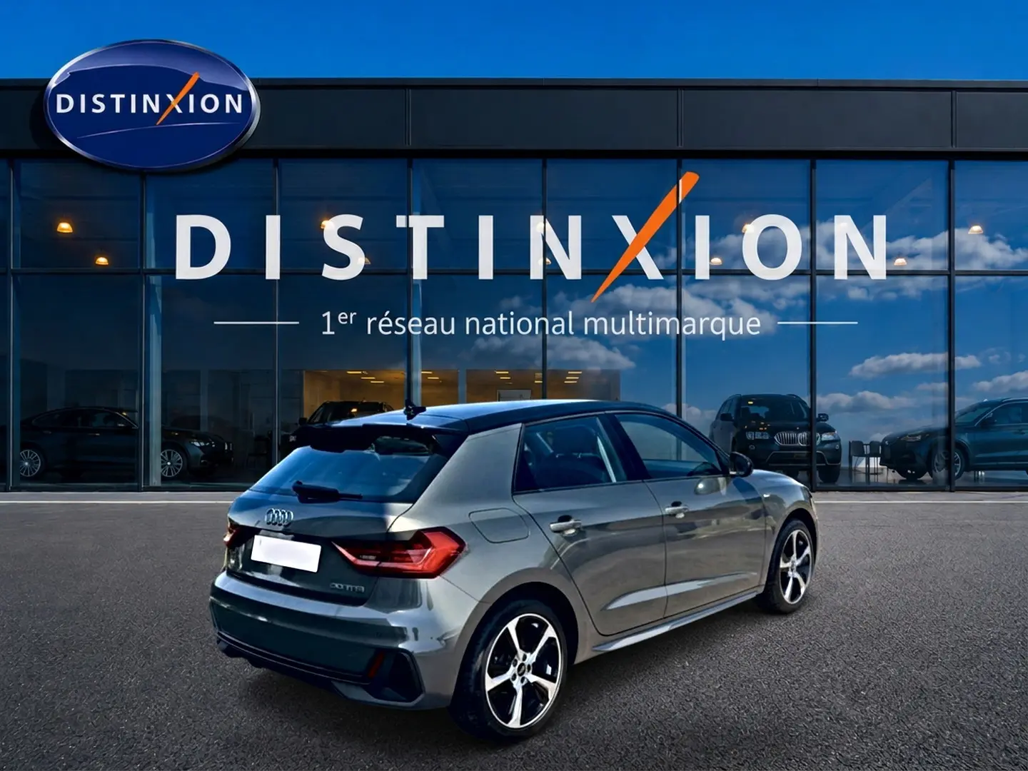 Audi A1 Sportback gris chronos vue 3/4 arrière droit avec jantes alu et becquet arrière, devant une vitrine Distinxion.