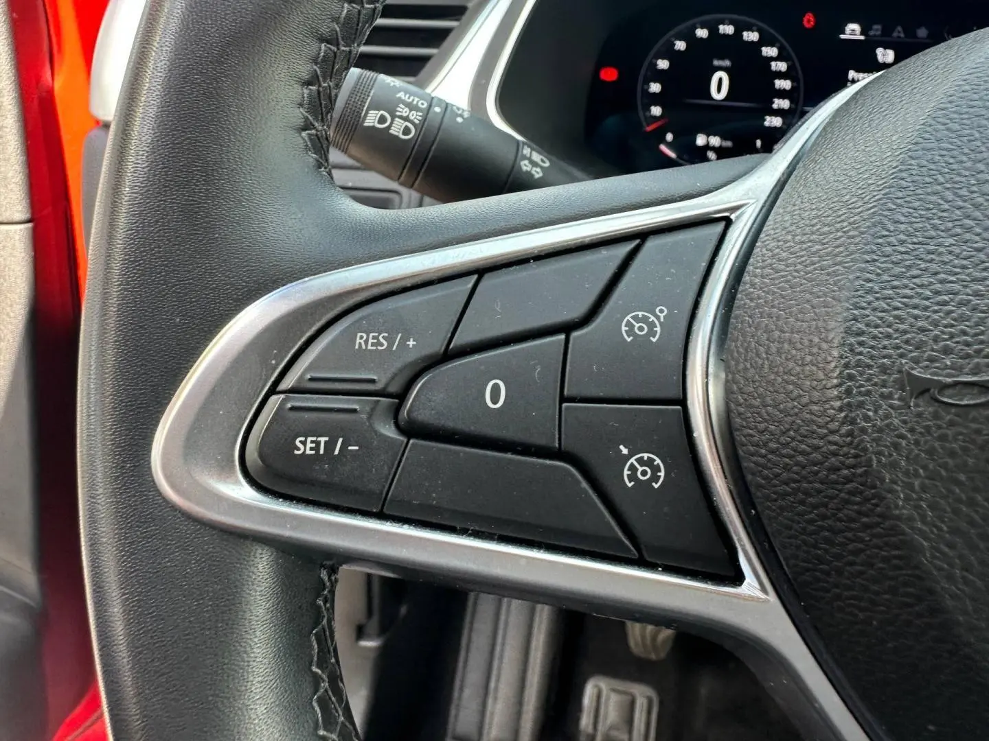 Gros plan sur les commandes du régulateur de vitesse au volant d’un Renault Captur rouge Flamme nacré 2024.