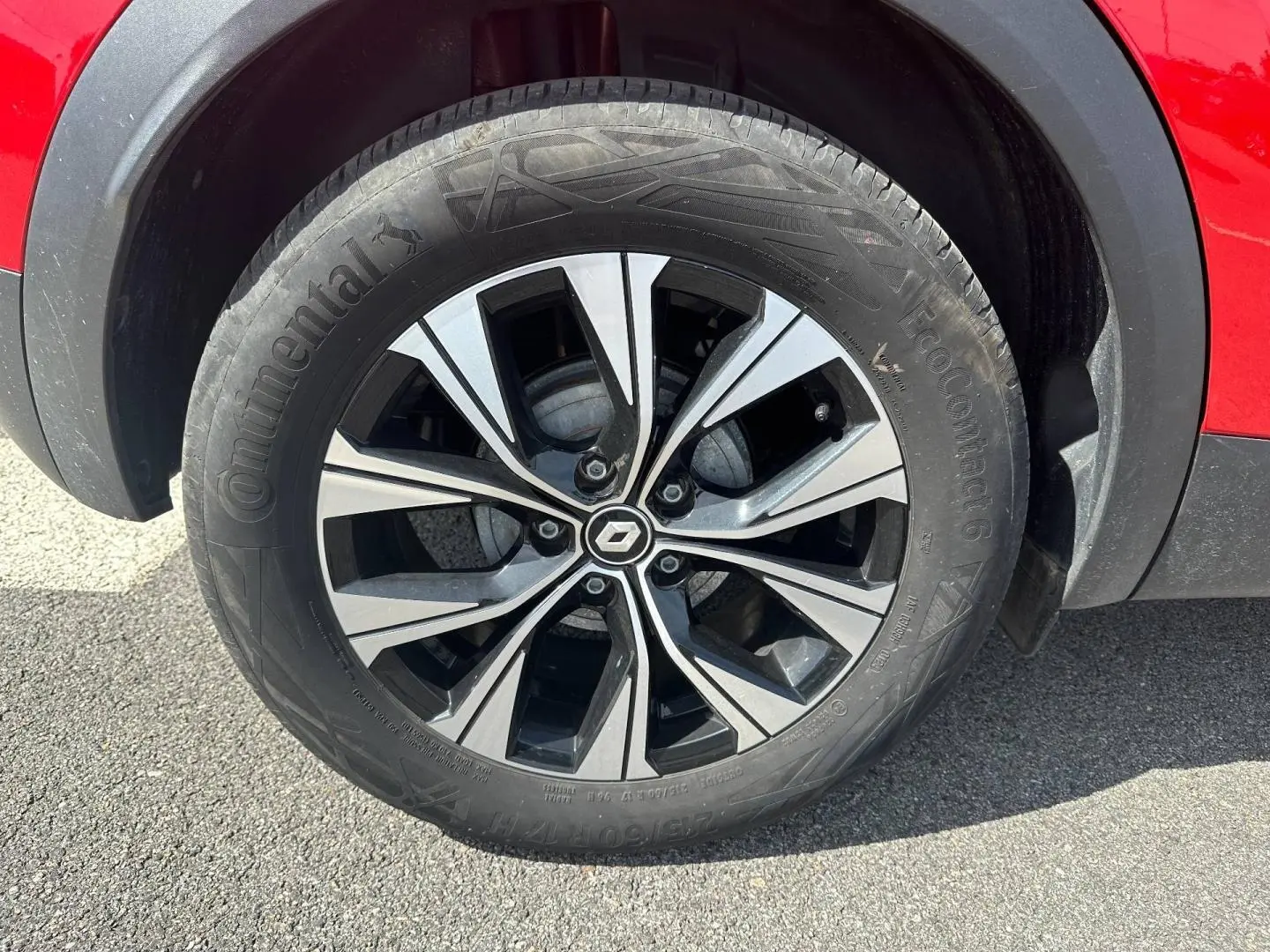 Gros plan sur la roue avant gauche du Renault Captur rouge Flamme nacré avec jante alu bicolore et logo Renault central.
