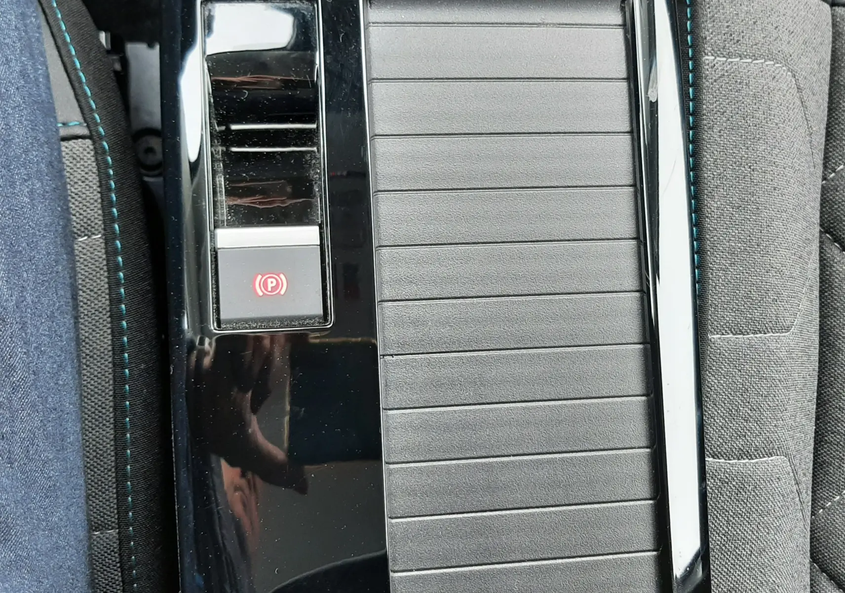 Gros plan sur la console centrale noire brillante de la Citroën C4 Hybrid 136, avec bouton frein à main électronique et surpiqûres bleues.