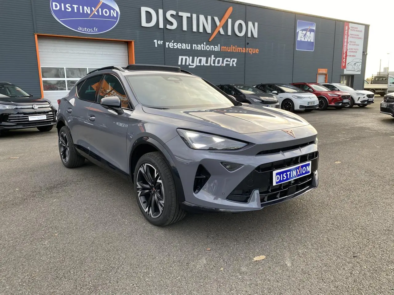 Vue 3/4 avant d’un CUPRA Formentor gris Graphène avec jantes noires et calandre marquée, stationné devant un concessionnaire.