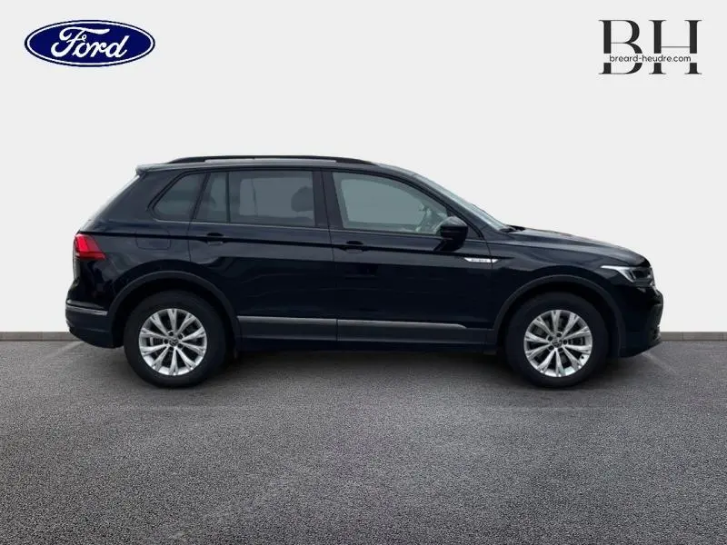 Profil côté gauche d'un Volkswagen Tiguan noir intense nacré, avec jantes alliage et barres de toit visibles.