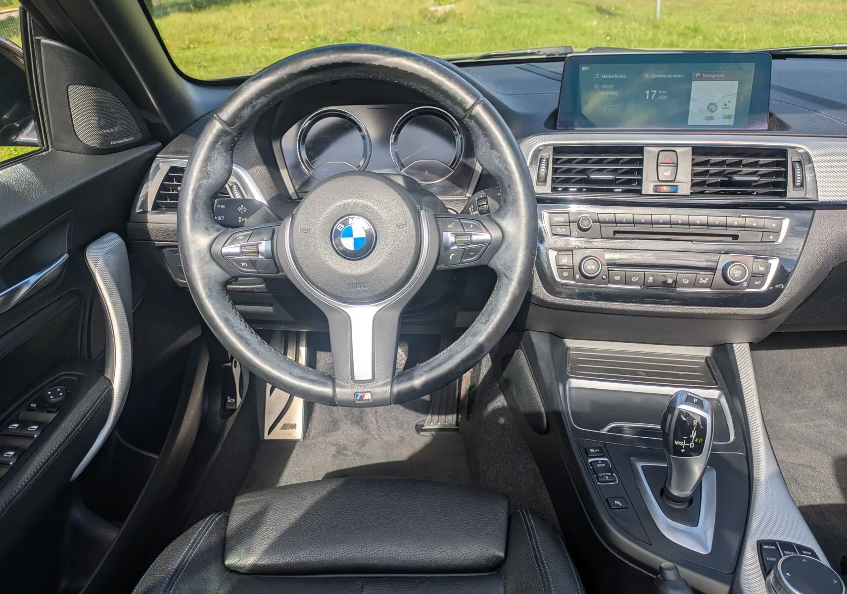 Vue intérieure centrée sur le volant et la console centrale d'une BMW Série 2 Cabriolet noire, avec écran tactile et levier de vitesse automatique.
