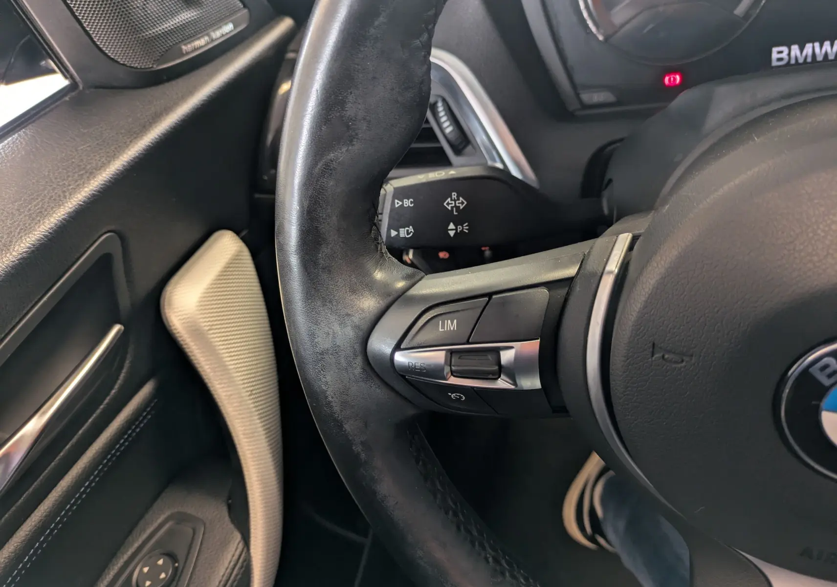 Gros plan sur le volant en cuir noir de la BMW Série 2 Cabriolet 218d, avec commandes intégrées et haut-parleur Harman Kardon.