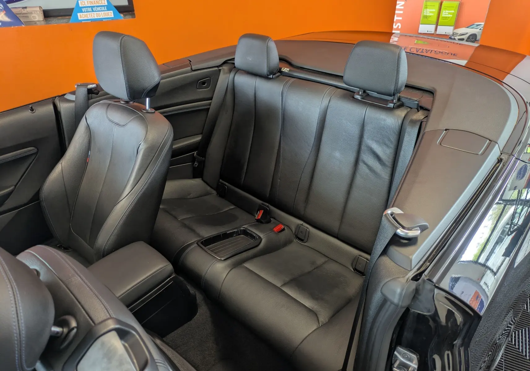 Vue intérieure arrière du cabriolet BMW Série 2 noir, mettant en valeur les sièges en cuir noir et l'habitacle ouvert.