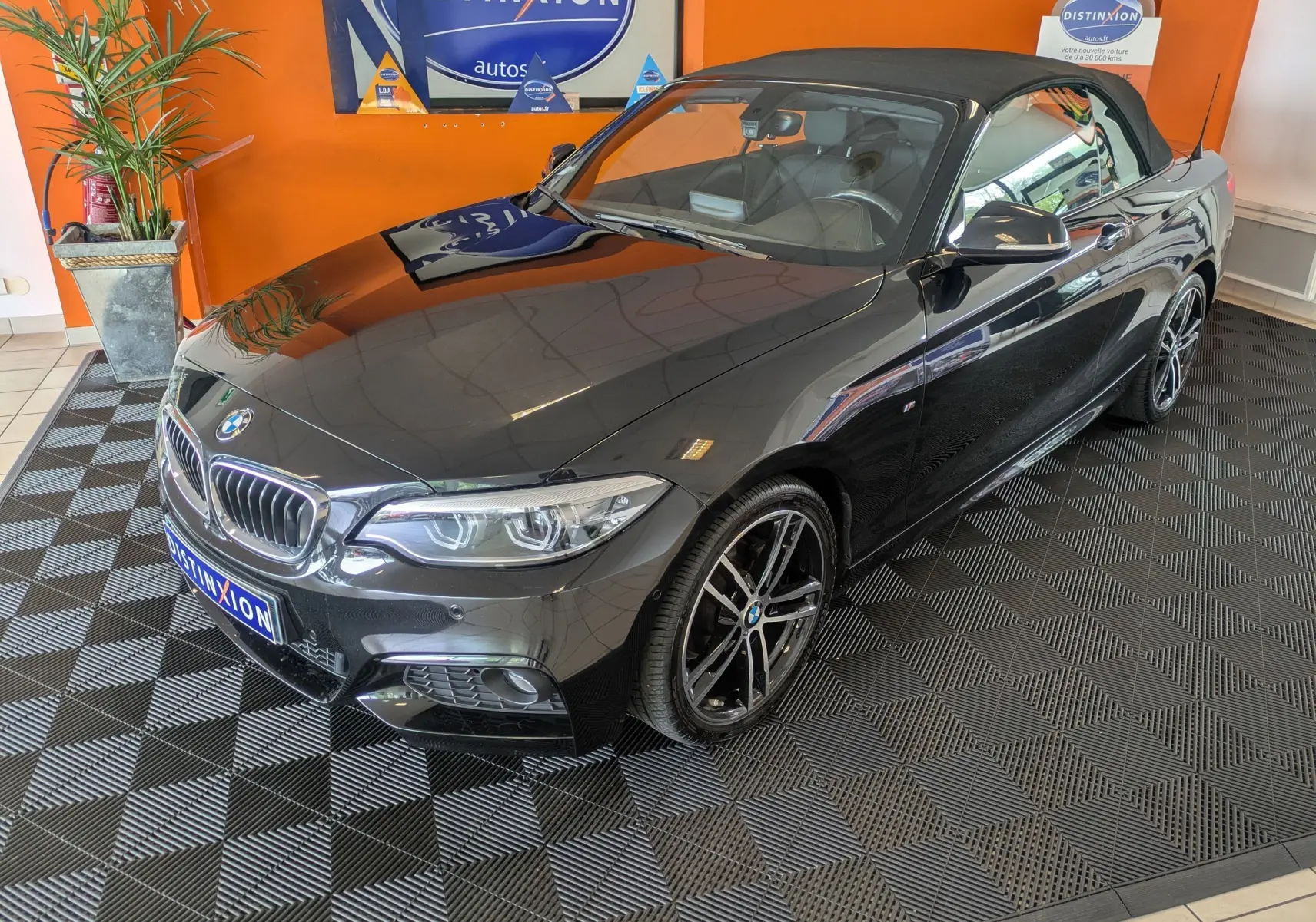 BMW Série 2 Cabriolet noir vue 3/4 avant droit, capote fermée, jantes alliage bicolores et intérieur cuir noir visible.