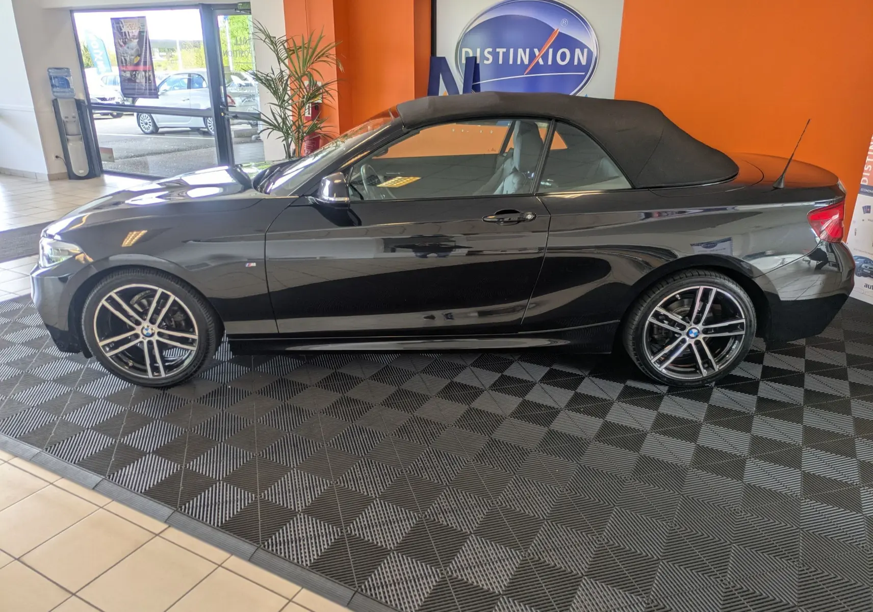 BMW Série 2 Cabriolet 218dA noir vue de profil côté gauche, toit souple fermé et jantes 18 pouces bicolores.