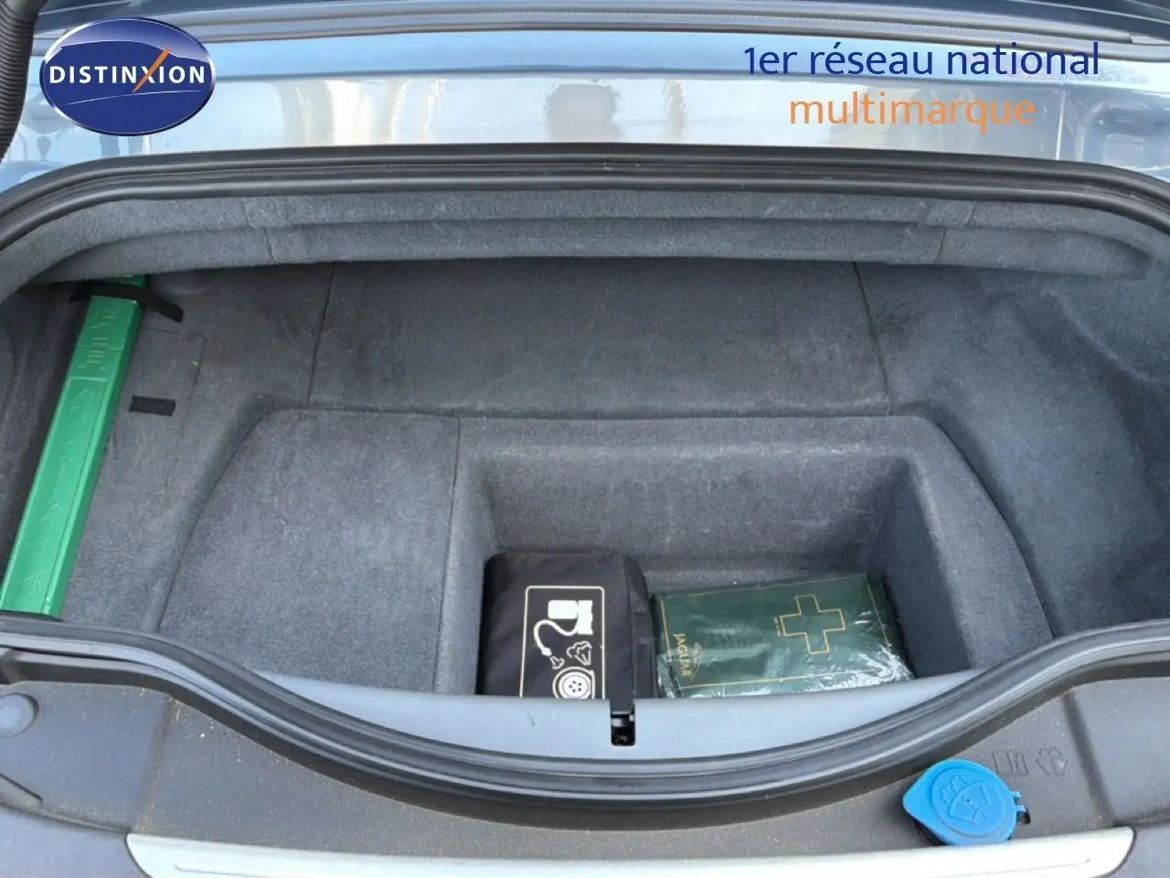 Coffre ouvert d’une Jaguar F-TYPE gris 2013, vue plongeante montrant un rangement avec trousse de secours et kit de réparation.