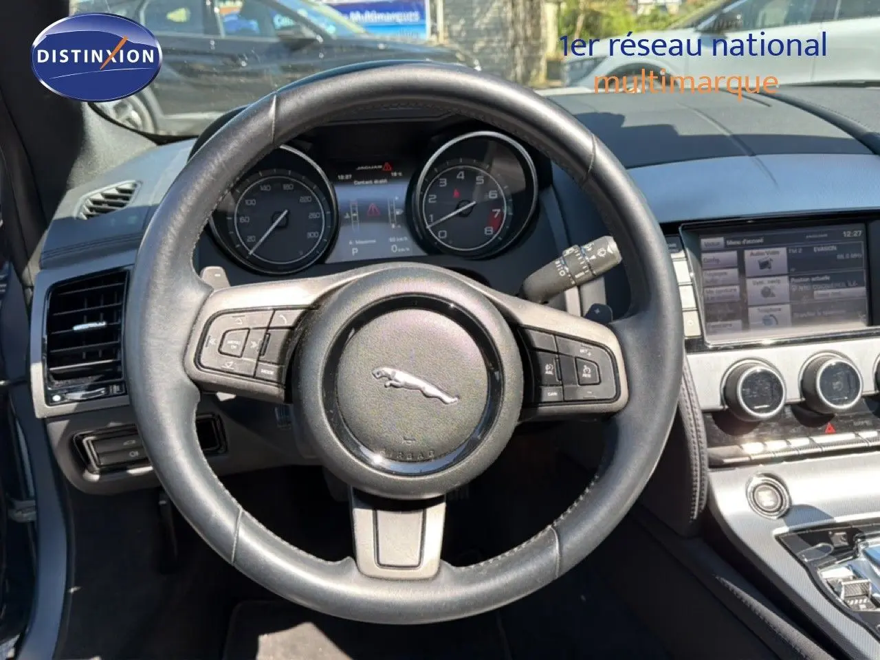 Vue intérieure centrée sur le volant en cuir noir de la Jaguar F-TYPE 3.0 V6, avec tableau de bord et console centrale visibles.