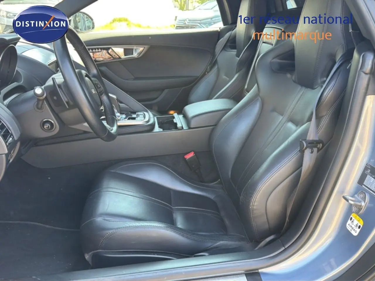 Vue intérieure côté conducteur de la Jaguar F-TYPE 3.0 V6 gris, sièges sport cuir noirs et console centrale visible.