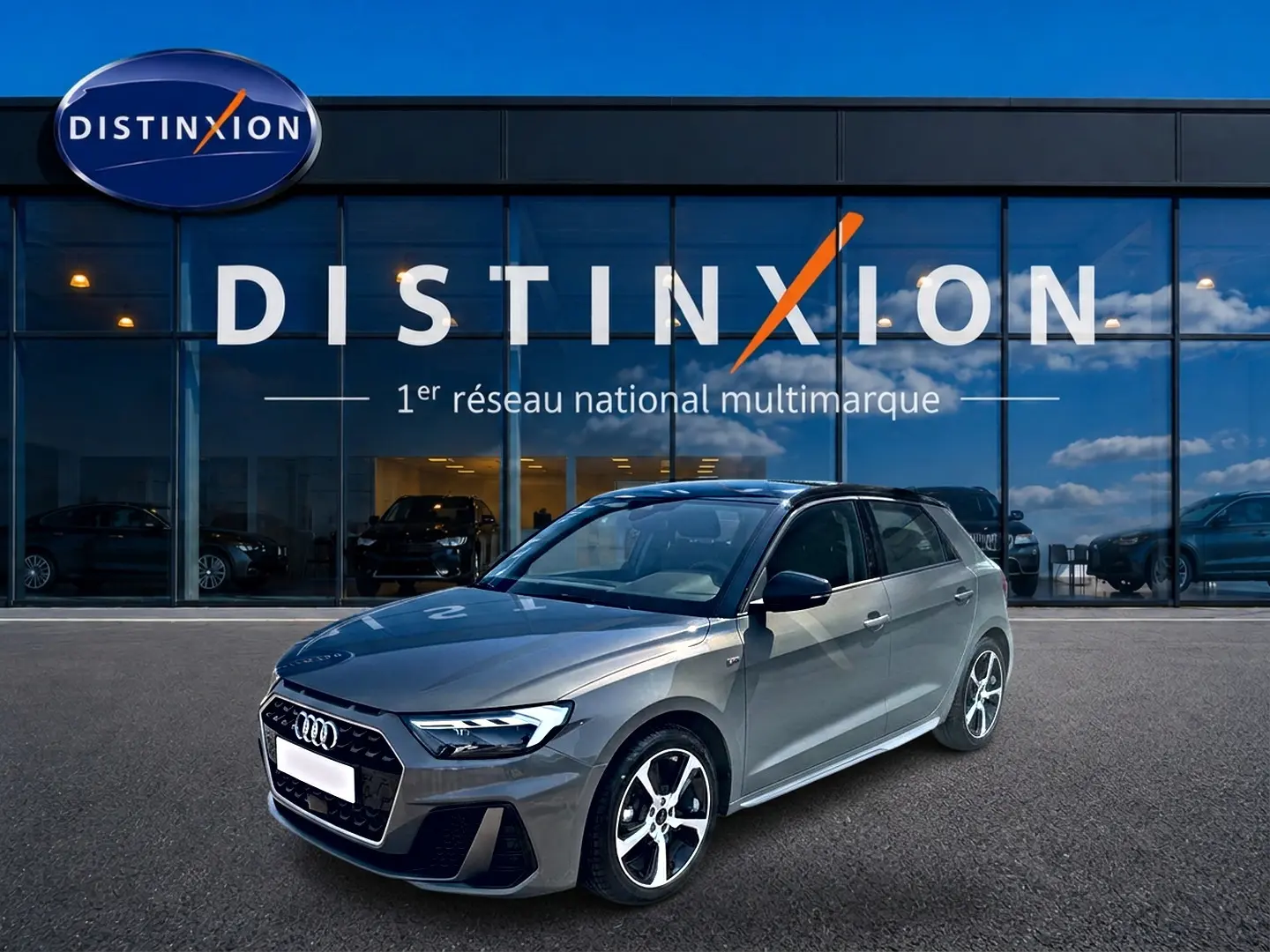 Audi A1 Sportback gris chronos vue 3/4 avant droit avec toit noir et jantes alu distinctives devant un showroom Distinxion.