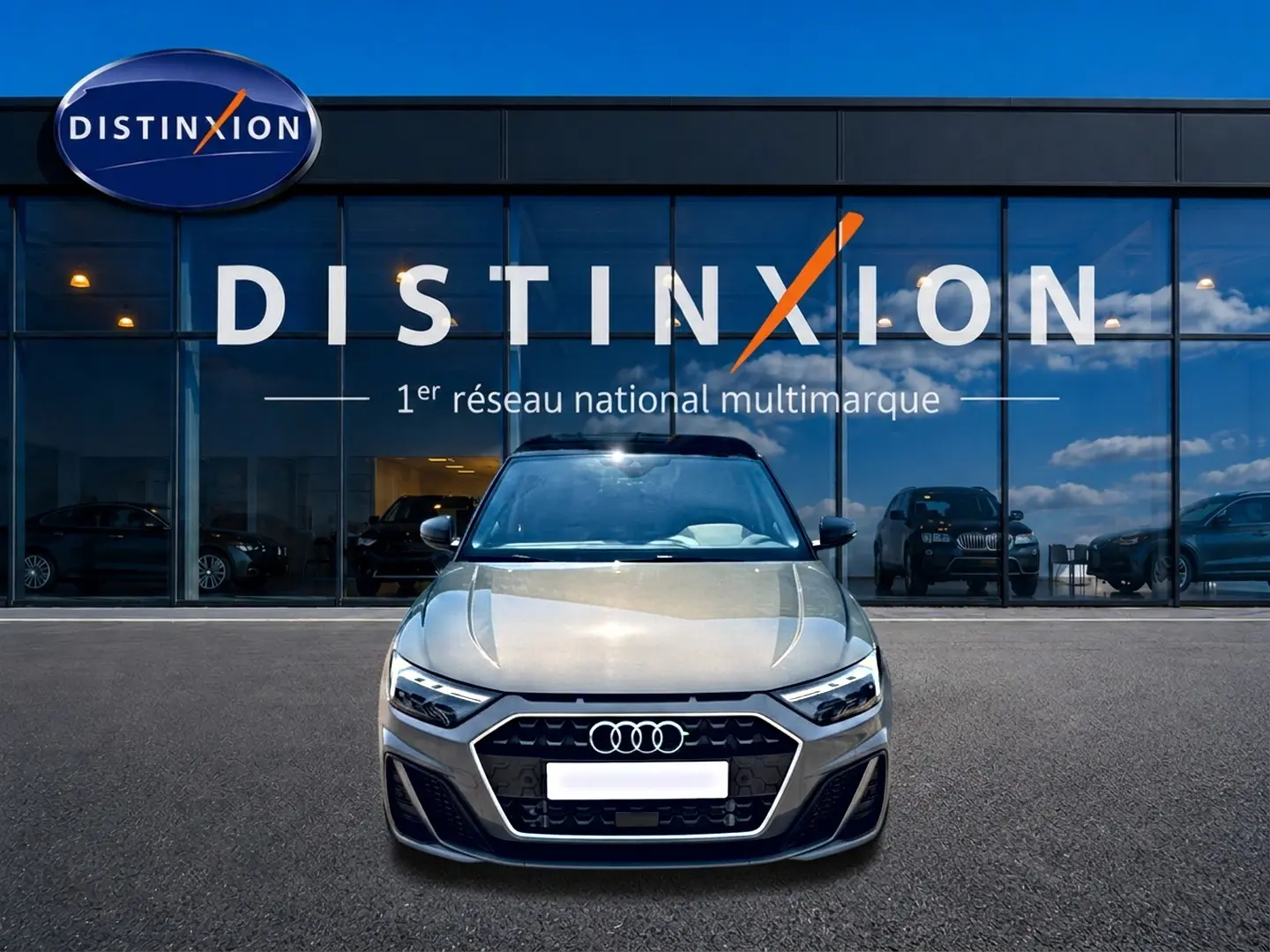 Audi A1 Sportback gris chronos vue de face, avec calandre noire et phares LED devant un showroom Distinxion.