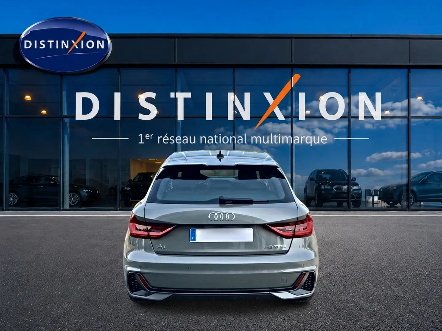 Vue arrière d'une Audi A1 Sportback gris chronos avec feux LED et becquet arrière, stationnée devant une vitrine Distinxion.