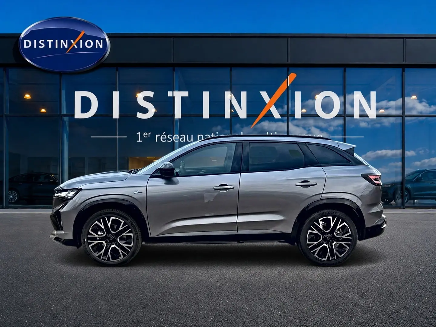 Profil droit du Renault Austral gris schiste 2026 devant une vitrine avec logo Distinxion visible.