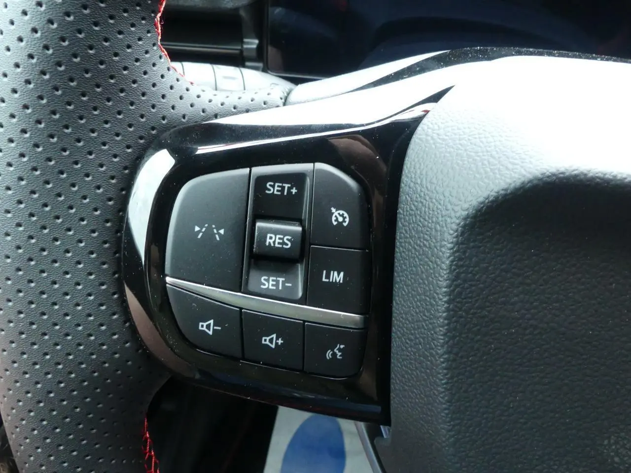 Gros plan sur les commandes de régulateur et volume au volant perforé avec surpiqûres rouges du Ford Puma gris métallisé 2025.