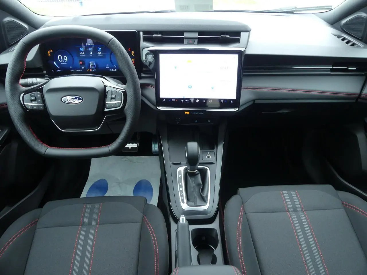 Intérieur Ford Puma 2025 vu de face, tableau de bord moderne avec écran tactile 12", volant et sièges noirs à surpiqûres rouges.