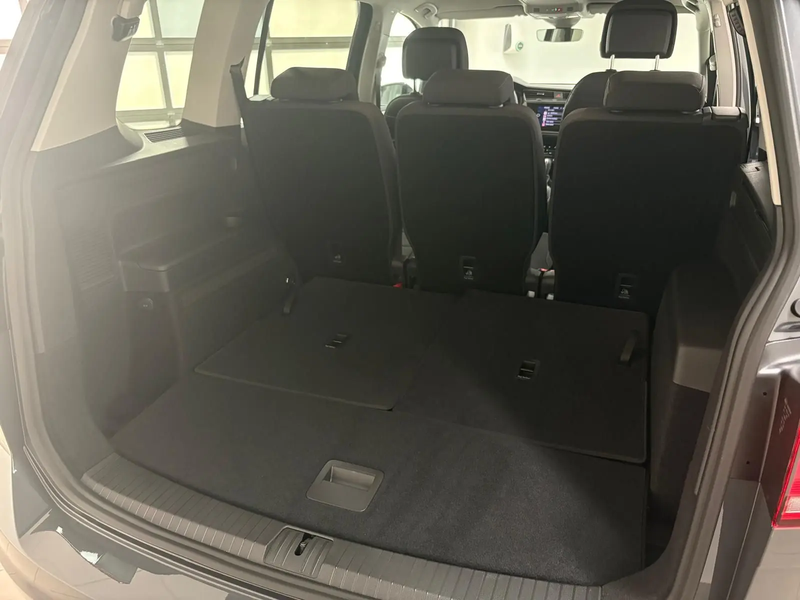 Vue arrière du coffre du Volkswagen Touran gris dauphin 2025 avec sièges rabattus et intérieur noir.