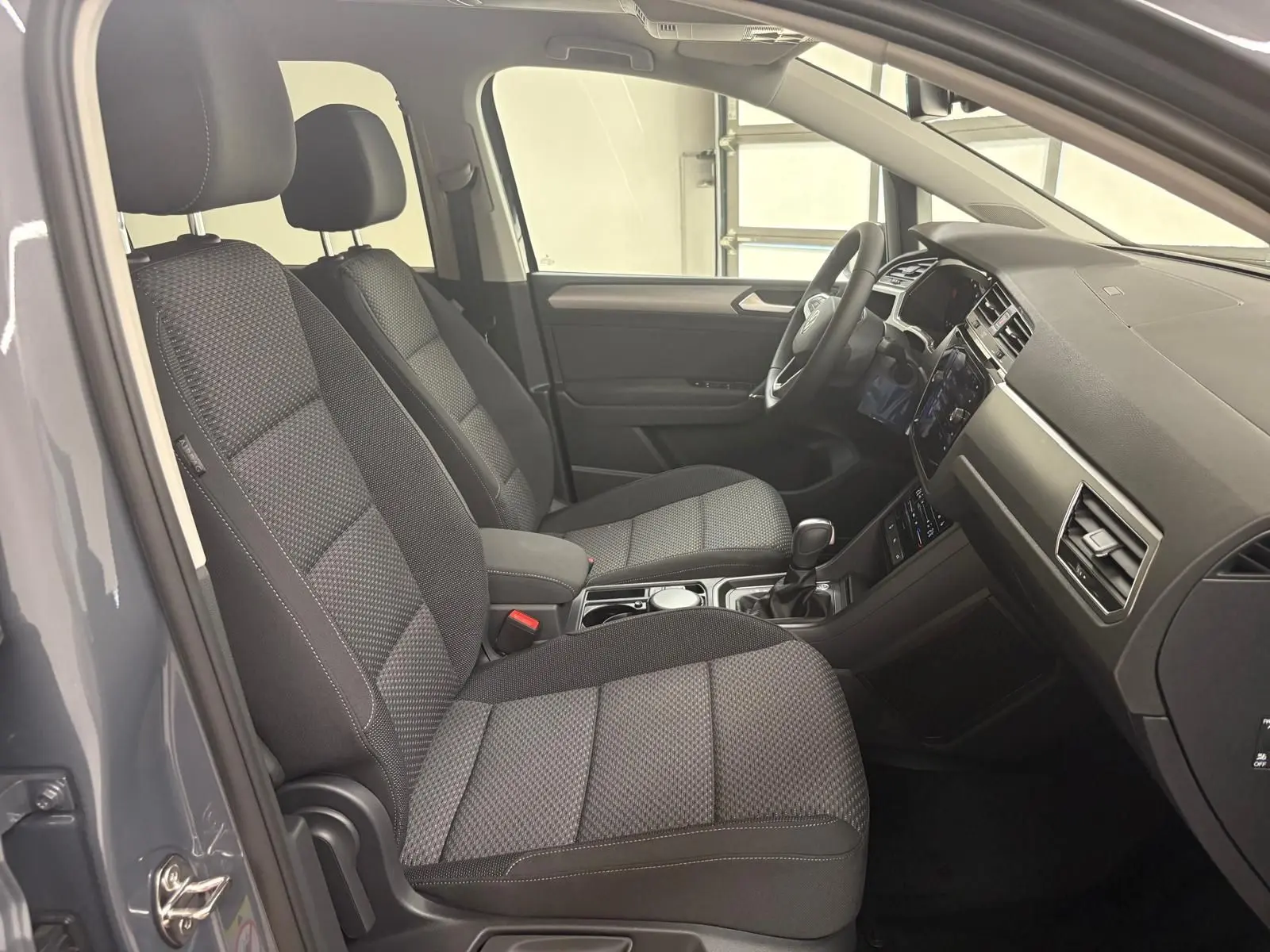 Intérieur avant du Volkswagen Touran gris dauphin 2025, sièges tissu gris et tableau de bord moderne côté droit.