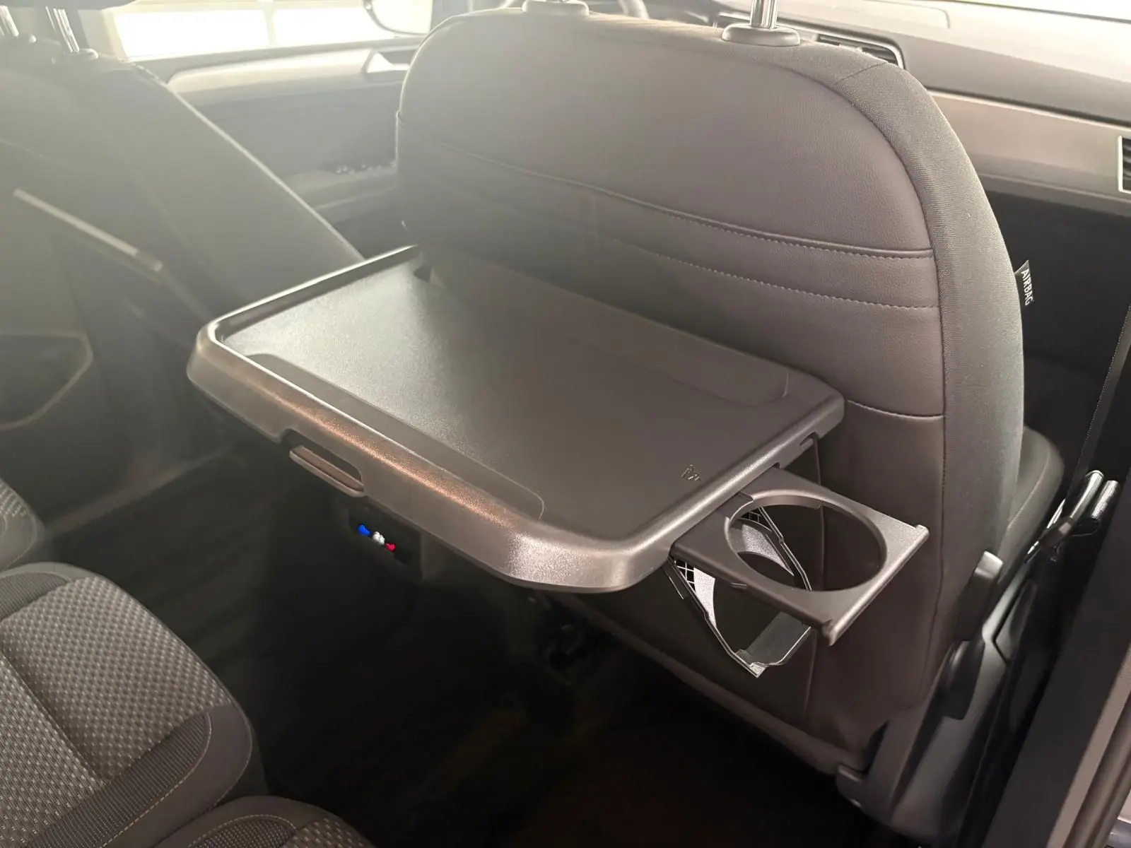 Tablette rabattable avec porte-gobelet sur le dossier du siège avant dans l'habitacle gris du Volkswagen Touran 2025.