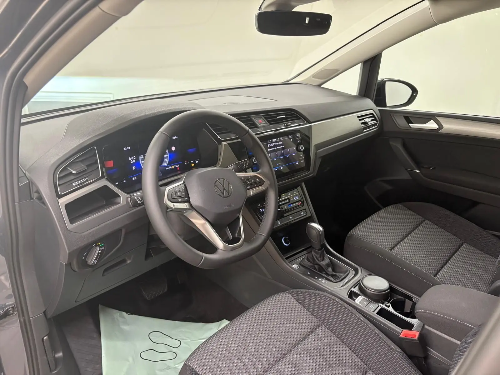 Intérieur du Volkswagen Touran gris dauphin 2025, vue côté conducteur montrant le tableau de bord et la console centrale moderne.