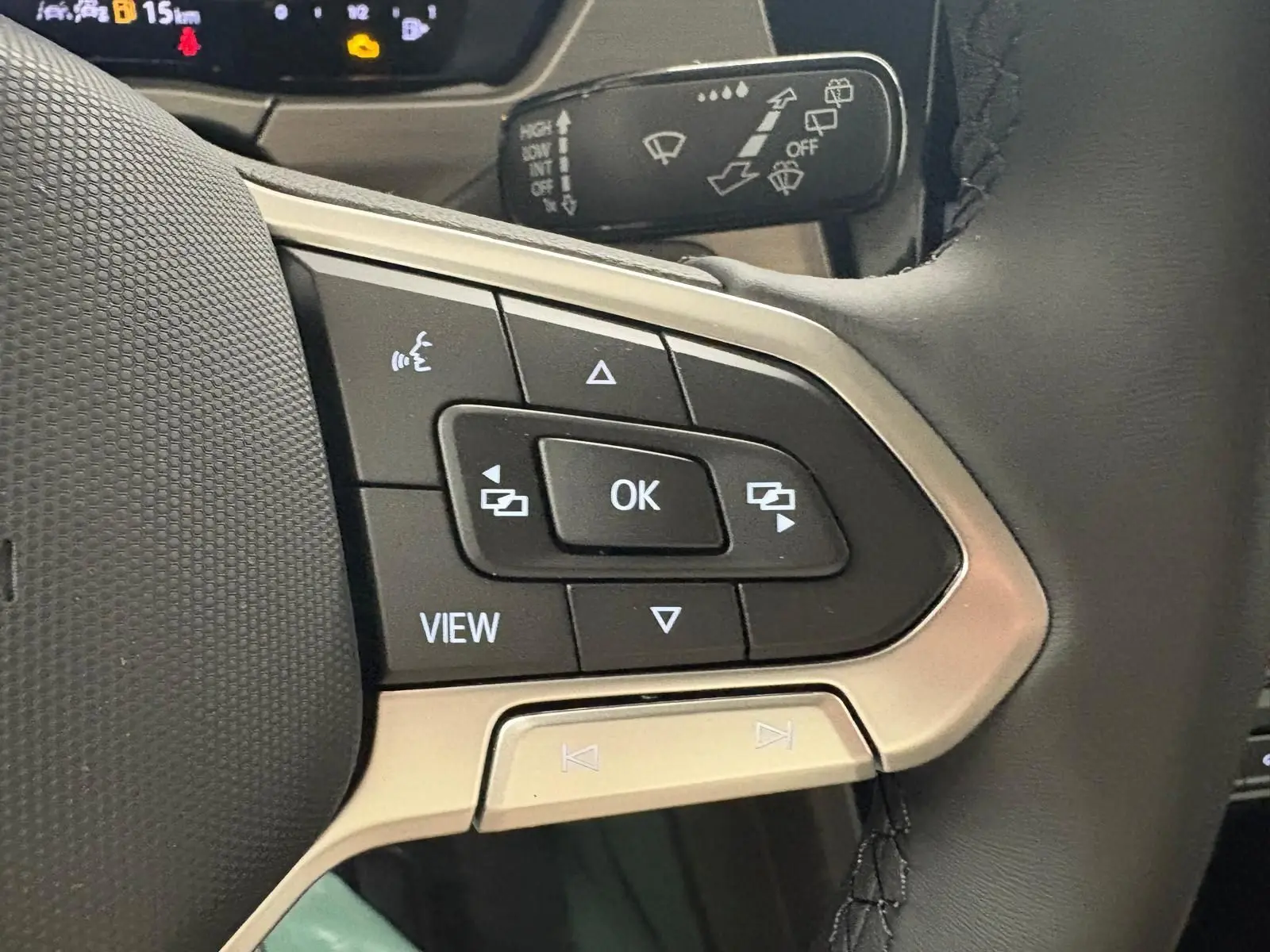 Gros plan sur les commandes multifonctions à gauche du volant cuir du Volkswagen Touran gris Dauphin 2025.