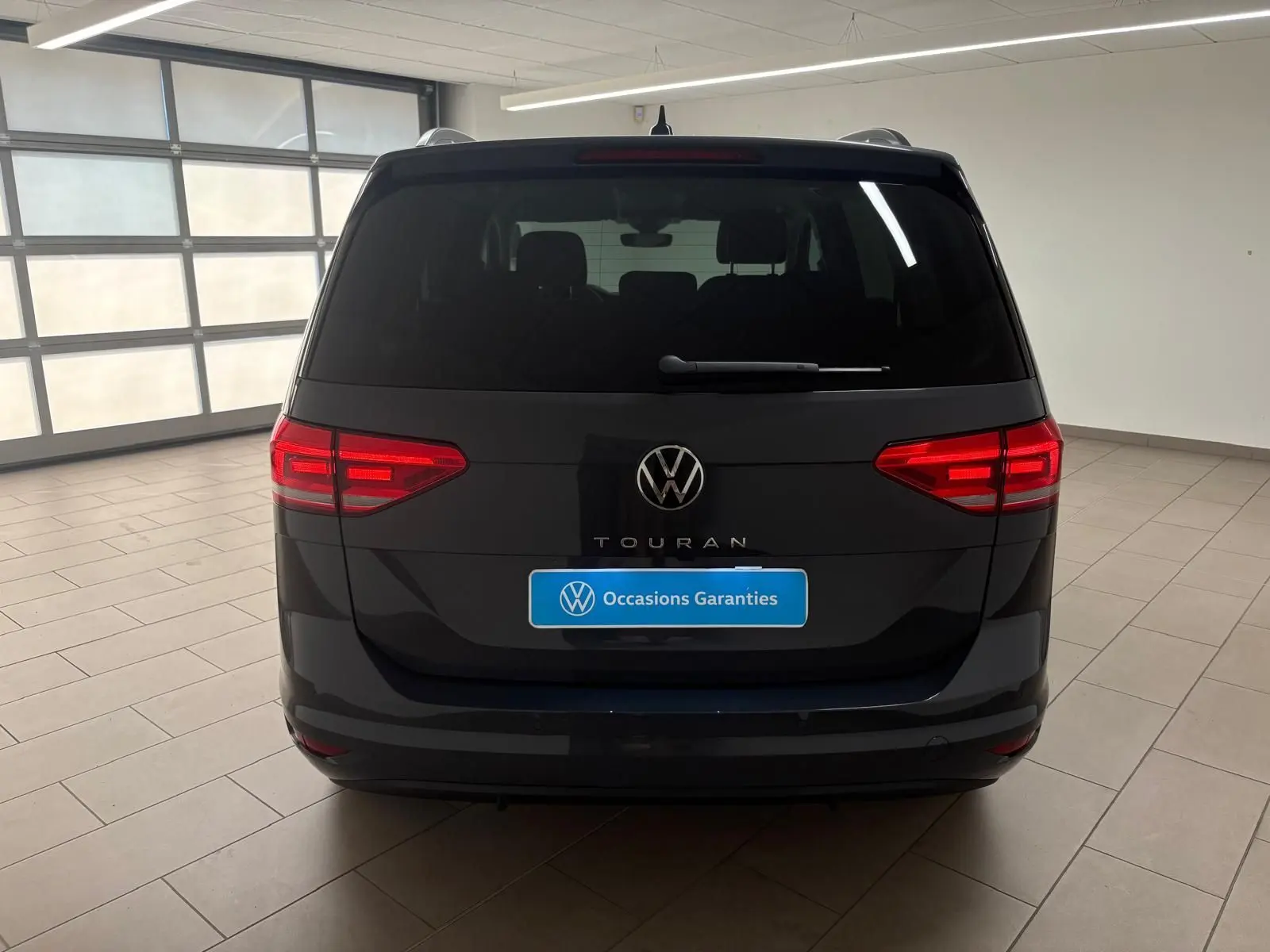 Vue arrière d'un Volkswagen Touran gris dauphin 2025 avec feux LED et logo VW bien visibles dans un garage.