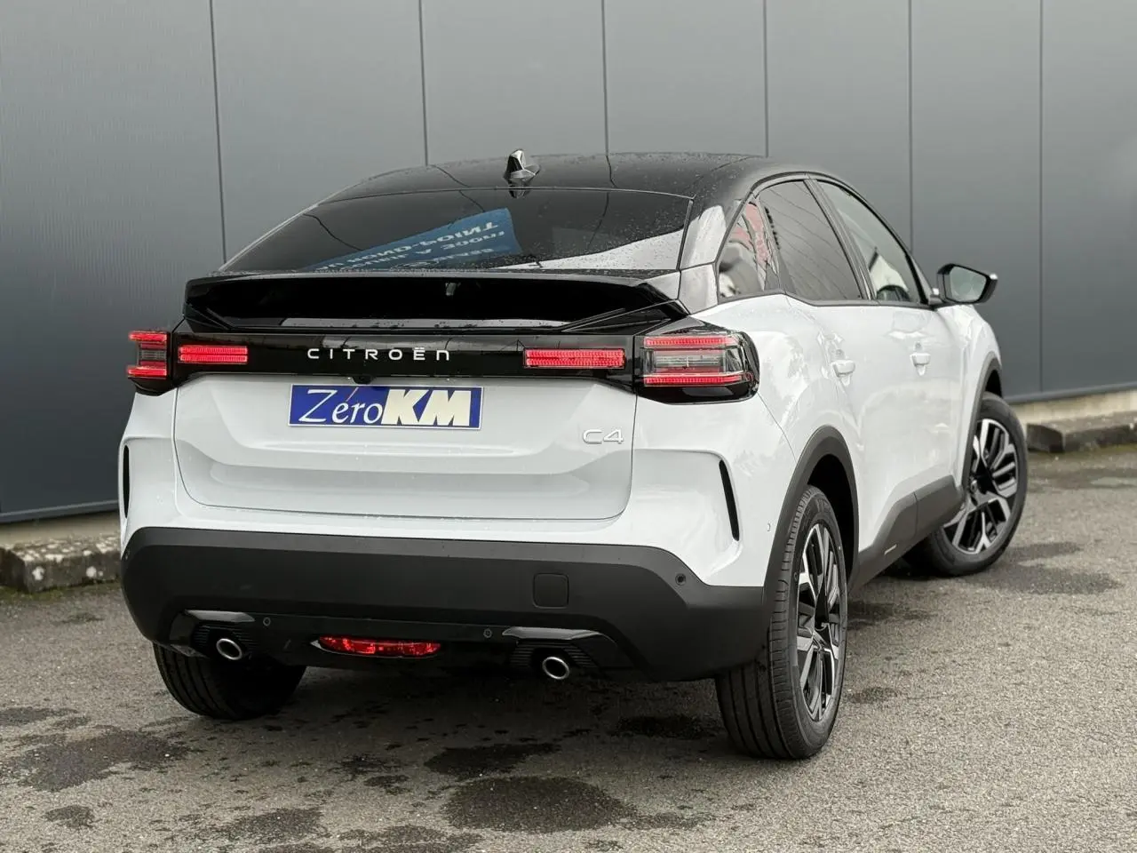 Vue 3/4 arrière droite d'une Citroën C4 blanche Okénite avec toit noir et feux arrière LED allumés.