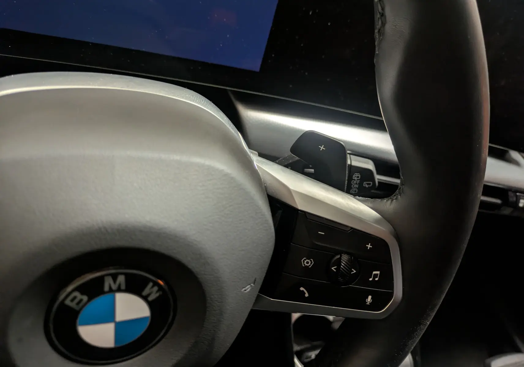 Gros plan sur le volant cuir M de la BMW X1 blanc, avec commandes multifonctions et palettes au volant visibles.
